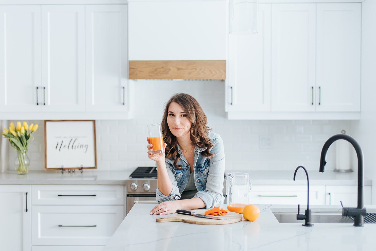 Founder, Ewa Reid, leaning on a kitchen counter and holding a glass of fresh squeezed orange juice.